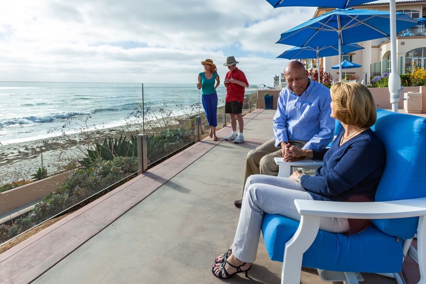 Senior couple sitting in chairs on a patio while another senior couple stands in the background