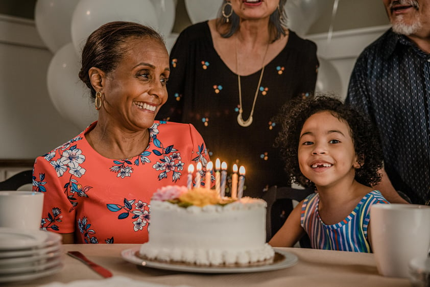 Senior woman sitting in front of a birthday cake and surrounded by friends and family