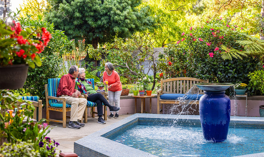 Senior woman standing and talking to a senior couple sitting in an outdoor seating area at Piedmont Gardens