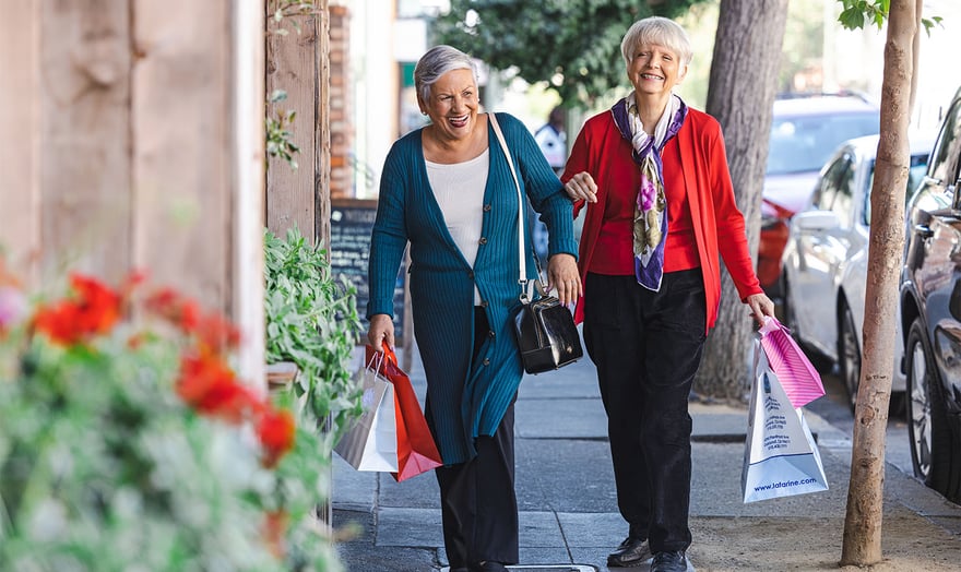 Two senior women walking through town while holding shopping bags