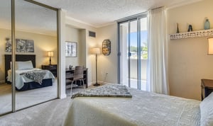 Bedroom of an apartment at Piedmont Gardens with a bed, desk and mirrored closet doors