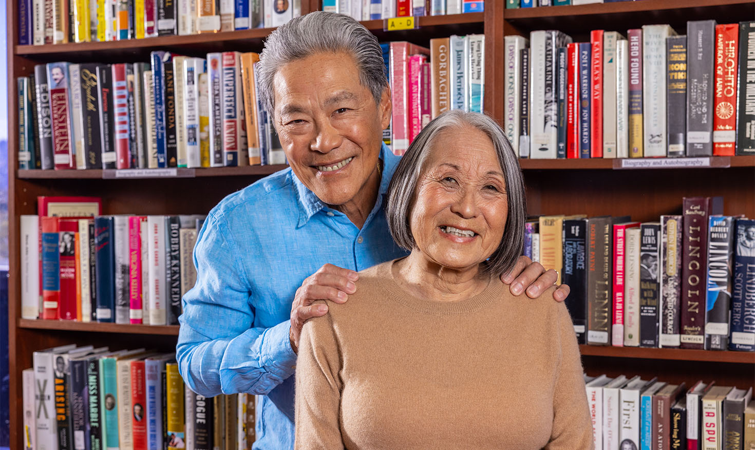 Senior man with his hands on the shoulders of a senior woman standing in front of bookshelves in the Piedmont Gardens library