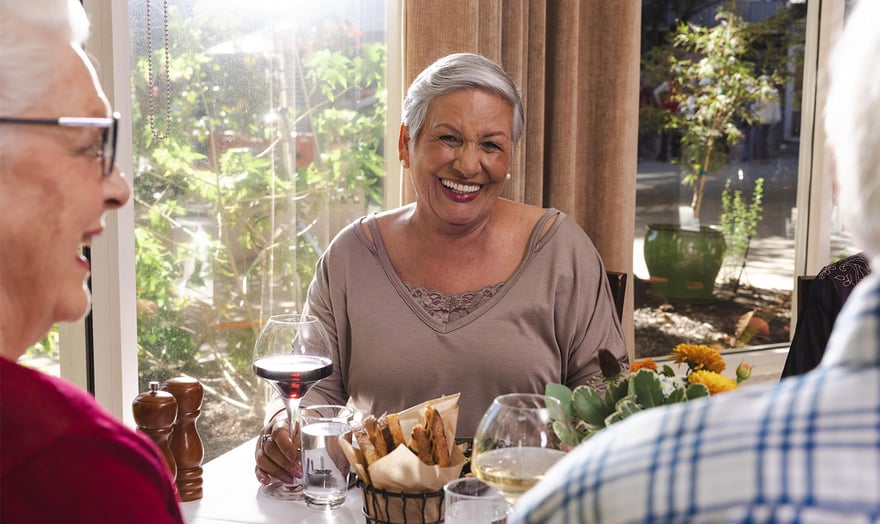 Senior woman holding a glass of red wine and enjoying a meal with friends in the Piedmont Gardens dining venue