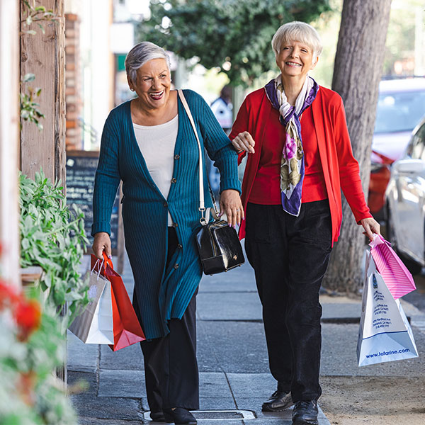 Two senior women walking through town while holding shopping bags