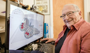 Senior man sitting in front of a computer that's showing a 3D rendering