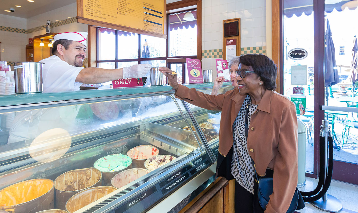 Senior woman receiving a sample of ice cream from an employee at an ice cream parlor