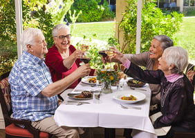 Three senior women and a senior man toasting with wine glasses and enjoying a meal on the patio