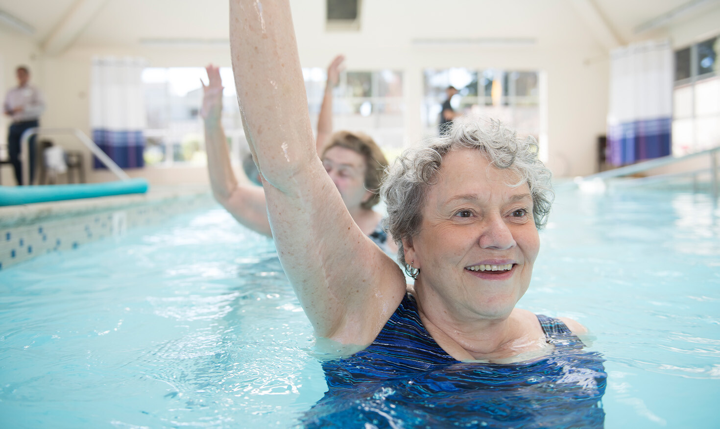 Senior woman doing water aerobics in an indoor pool at Redwood Terrace with more seniors in the background