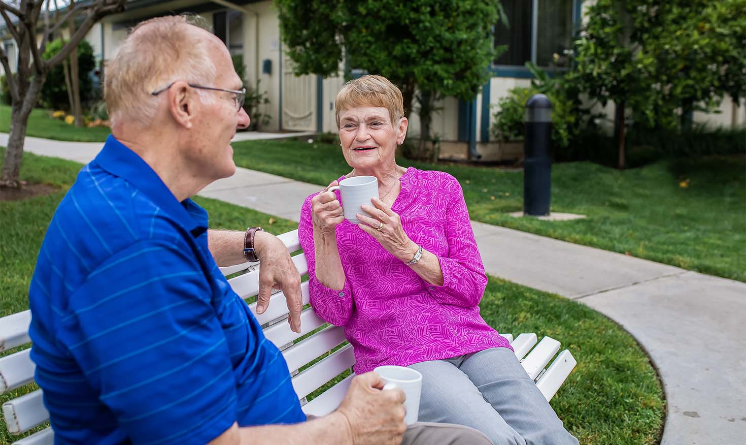 Senior couple drinking coffee on a bench outside at Redwood Terrace