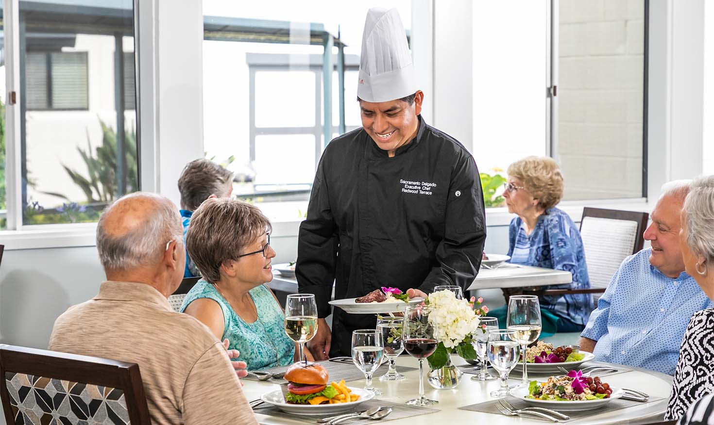 Redwood Terrace chef presenting a plate of food to a senior resident in the community dining room