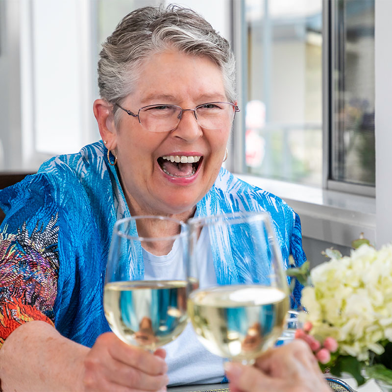 Senior woman clinking glass of white wine with another person at lunch at Redwood Terrace