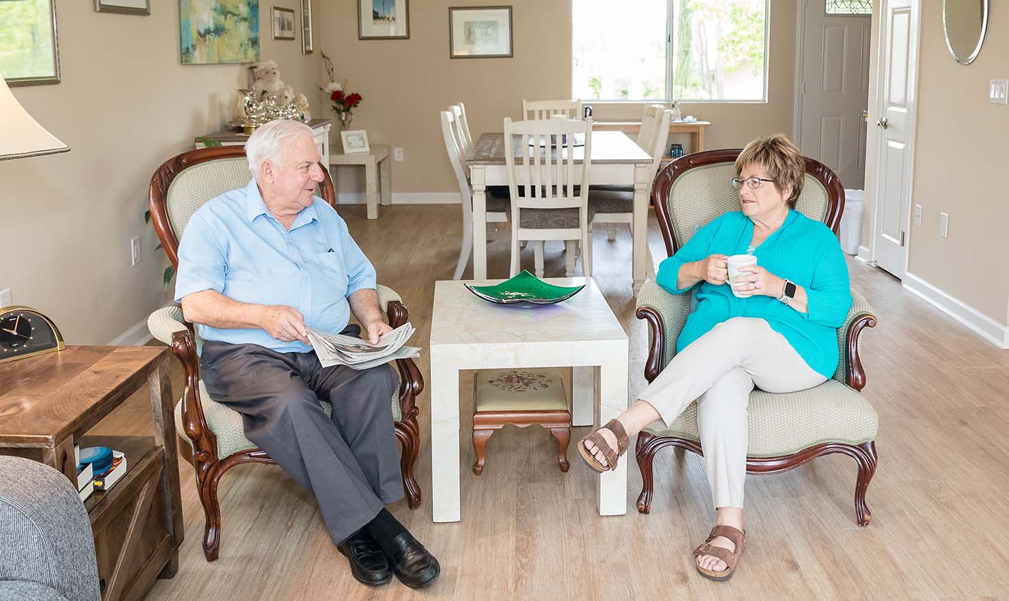 A senior man holding a newspaper and a senior woman holding a mug sitting inside their home at Redwood Terrace