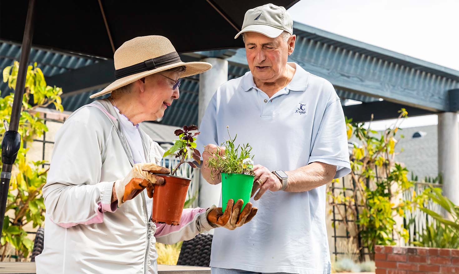 Senior man and woman holding small containers of plants in the garden at Redwood Terrace