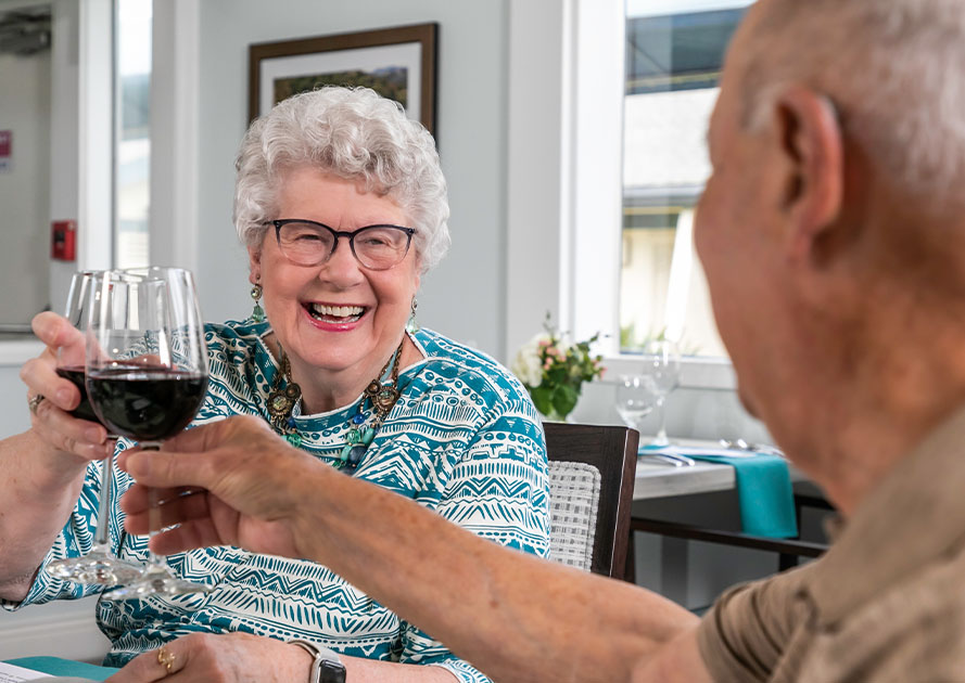 Senior couple clinking glasses of red wine in the dining room at Redwood Terrace