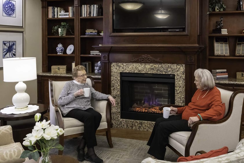 Two senior women having coffee together next to a fireplace at Rosewood