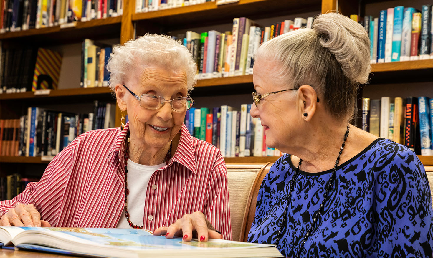 Two senior women looking at a book in the library at Rosewood
