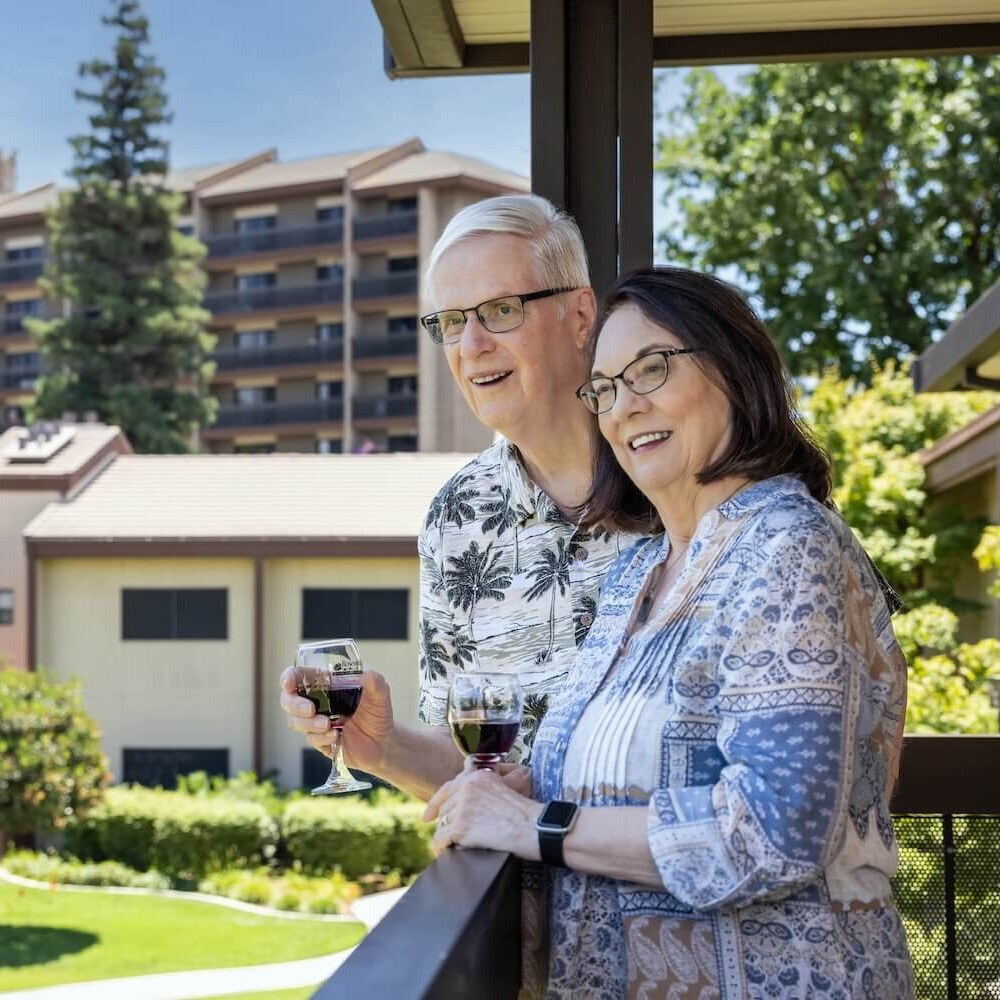 smiling couple standing on balcony with wine glasses