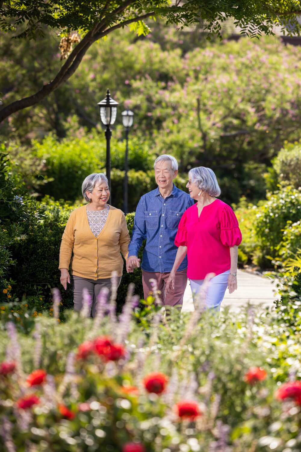 three smiling people walking through a garden
