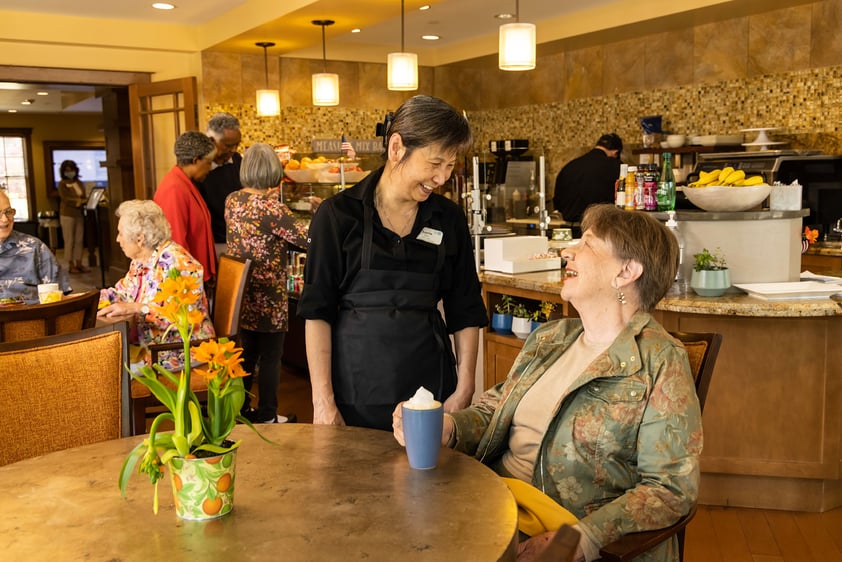 Team member talking to a senior woman sitting in The Terraces at Los Altos cafe