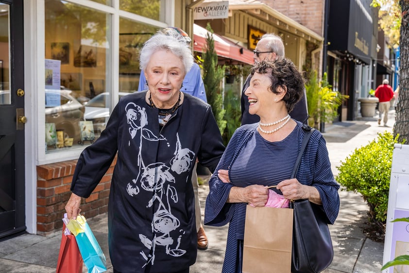 Two senior women walking arm and arm through downtown Los Altos and carrying shopping bags