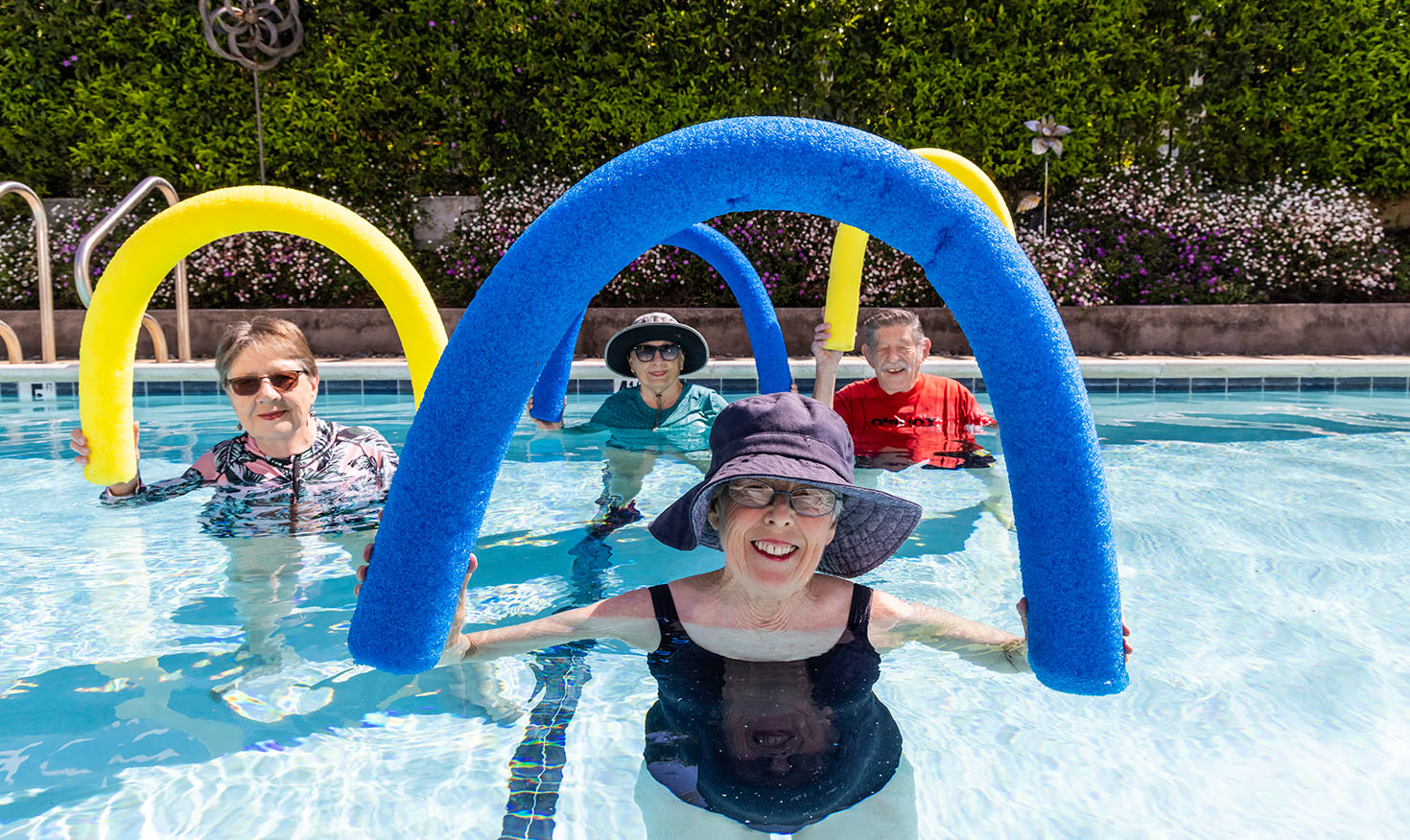 Group of four seniors in the pool holding up foam pool noodles