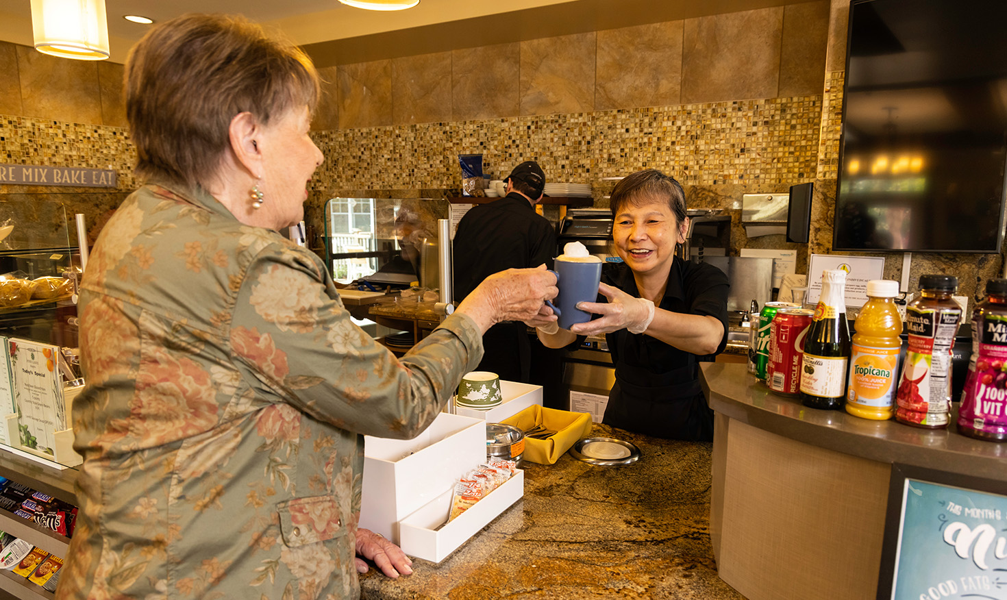 Cafe team member handing offer a mug to a senior woman in the community bistro