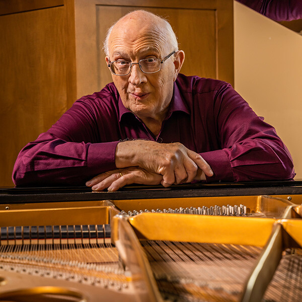 Senior man with his arms folded on top of a piano