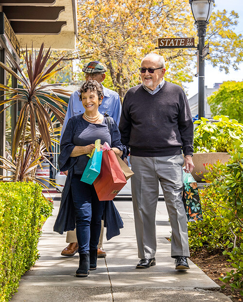 Two senior men and a senior woman holding shopping bags and walking through downtown Los Altos, California