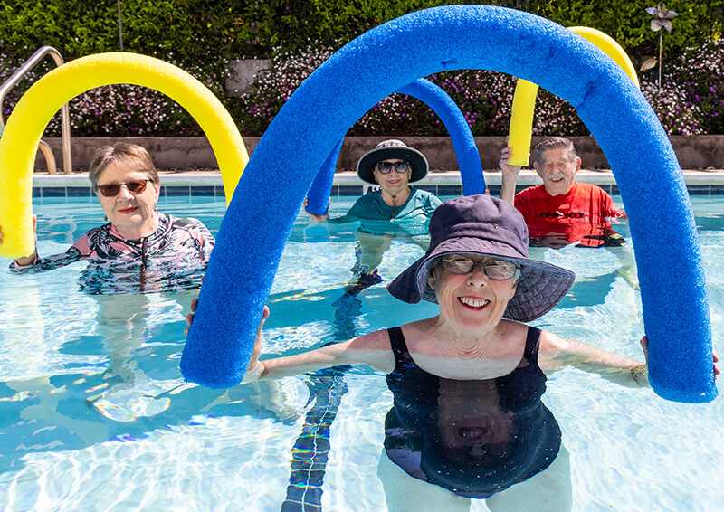 Group of four seniors in the pool holding up foam pool noodles