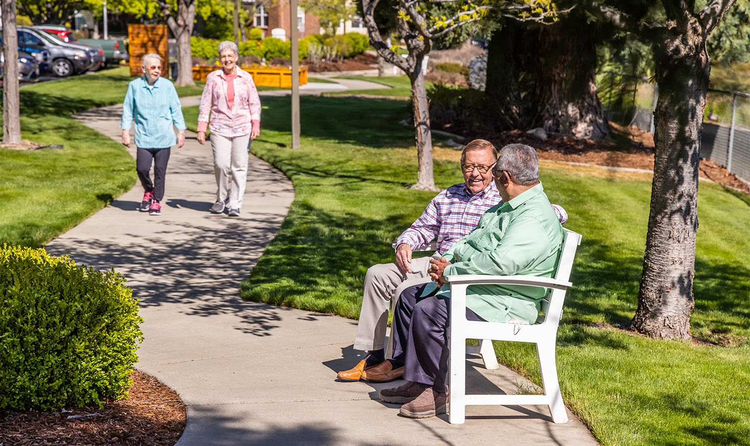 Two senior men sitting on a park bench and two senior women walking along the sidewalk