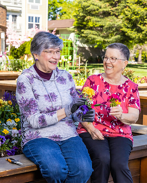 Two senior women holding flowers in the garden at The Terraces at Summitview