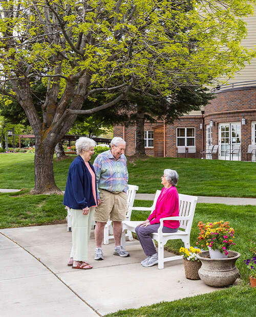 Senior woman on a park bench talking to a standing senior man and senior woman