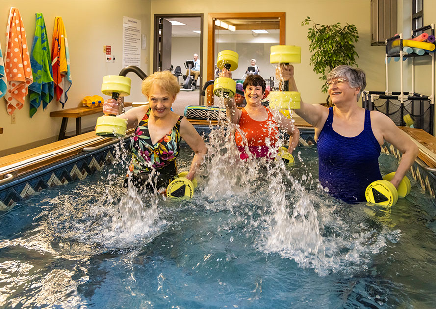 Three senior women using water weights in a water exercise class