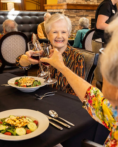 Two senior women toasting with wine glasses at lunch in The Terraces of Boise dining room