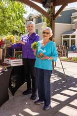 Two senior women holding up produce at a farmers market