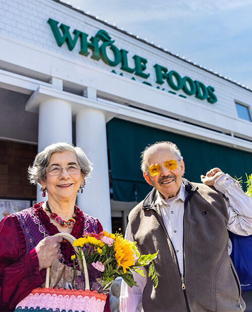 Senior couple walking out of a Whole Foods holding bags and a bouquet of flowers
