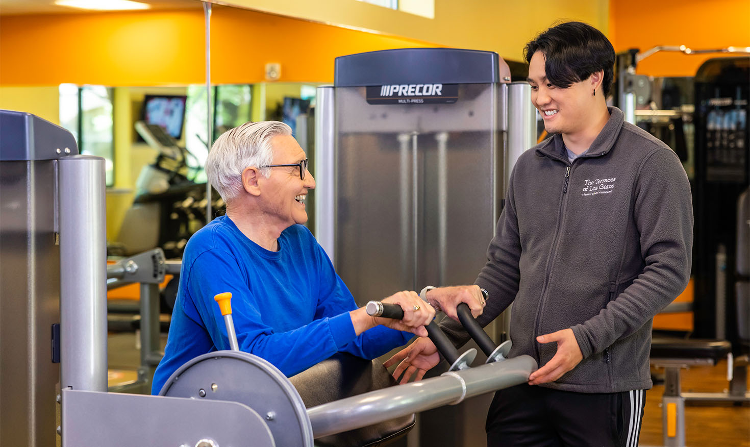 Senior man using a weight machine with the supervision of a personal trainer
