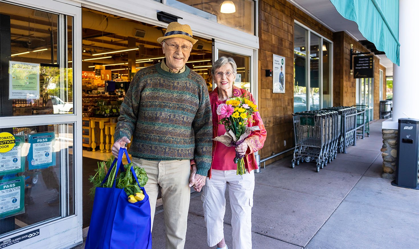 Senior couple walking out of a grocery store holding bags and a bouquet of flowers