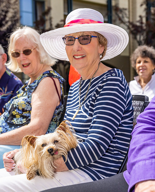 Senior woman wearing a sun hat while sitting and holding a small dog