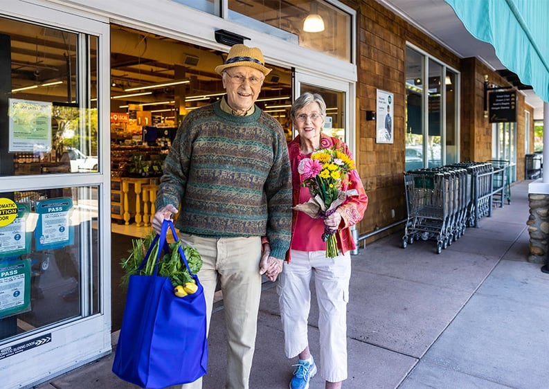 Senior couple walking out of a grocery store holding bags and a bouquet of flowers