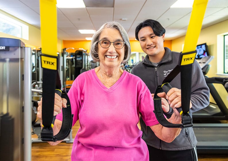 Senior woman working with TRX bands under the supervision of a personal trainer