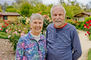 Smiling senior couple standing in front of rose bushes