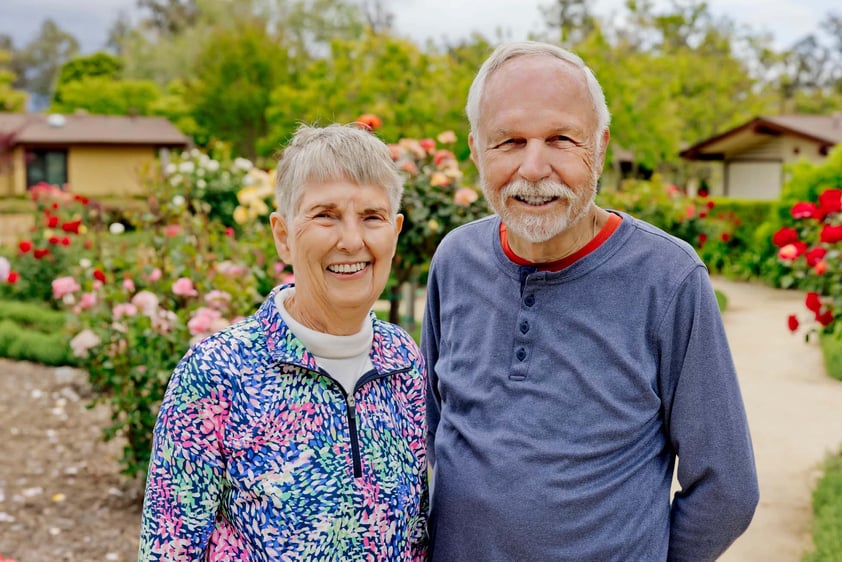 Smiling senior couple standing in front of rose bushes