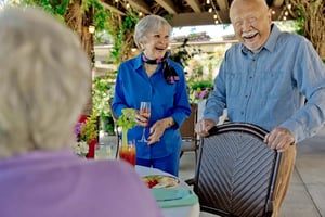 Smiling senior man and woman standing and talking to a senior woman sitting at an outdoor dining table