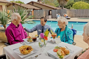 Valle Verde team member talking to a group of senior friends dining by the pool