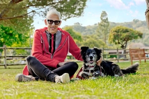 Senior woman sitting in the grass with her black-and-white dog