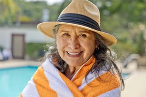 Senior woman in a hat standing by the pool wrapped in an orange and white striped towel