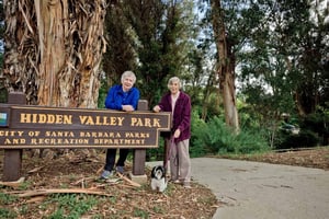 Two senior woman standing next to Hidden Valley Park sign with Havanese dog