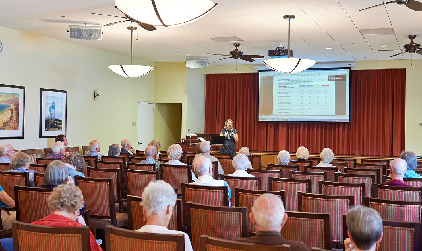 Seniors in the audience as a woman holding a microphone gives a presentation 