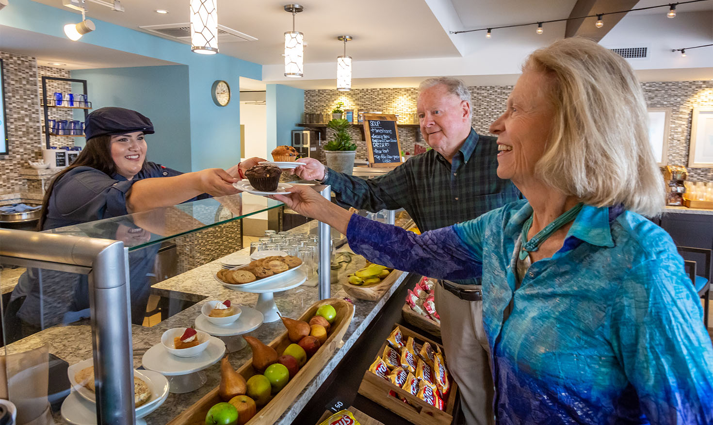 Cafe worker handing over muffins to a senior man and woman